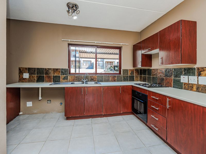 A functional kitchen featuring dark wood cabinetry, slate tile backsplash, built-in oven and hob, and tiled flooring, offering a blank canvas for renovation.