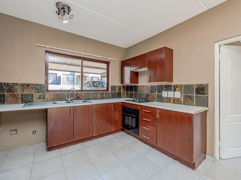 Functional kitchen featuring wooden cabinetry, slate tile backsplash, built-in oven and hob, and tiled flooring. The space is ready for a modern update.
