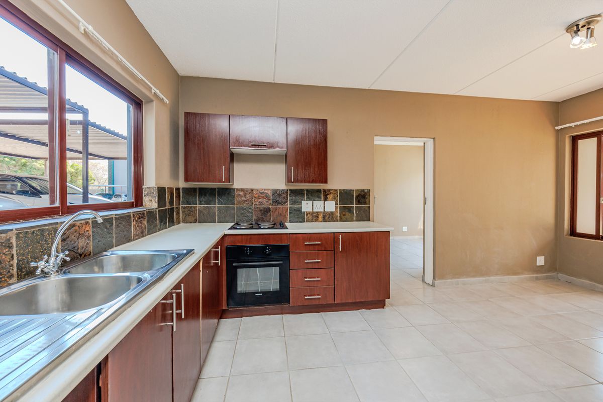 A functional kitchen featuring dark wood cabinetry, a built-in oven with hob, tiled splashback, and a double basin sink with tiled flooring.