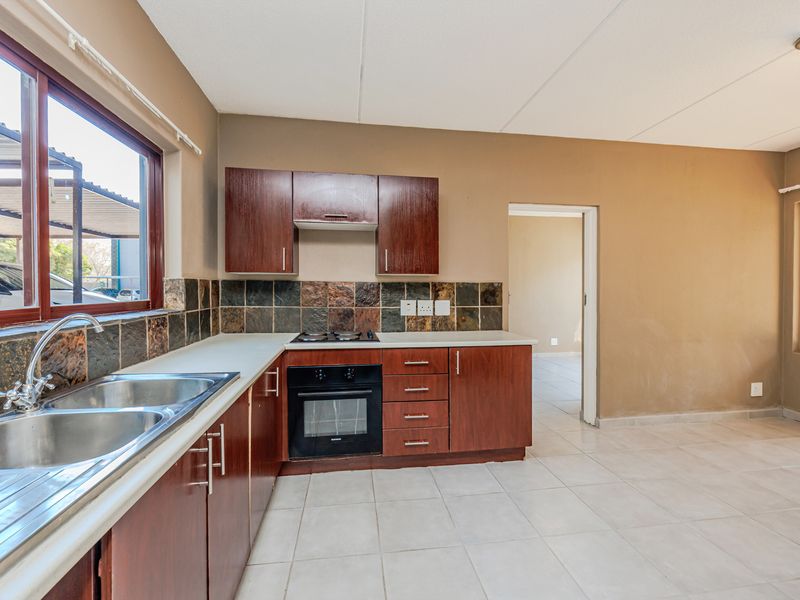 A functional kitchen featuring dark wood cabinetry, a built-in oven with hob, tiled splashback, and a double basin sink with tiled flooring.