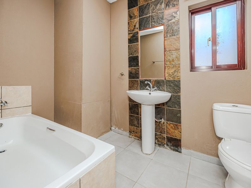 A functional bathroom featuring a pedestal basin, bathtub with shower mixer, and toilet, finished with a decorative stone-tiled splashback and neutral wall tones.