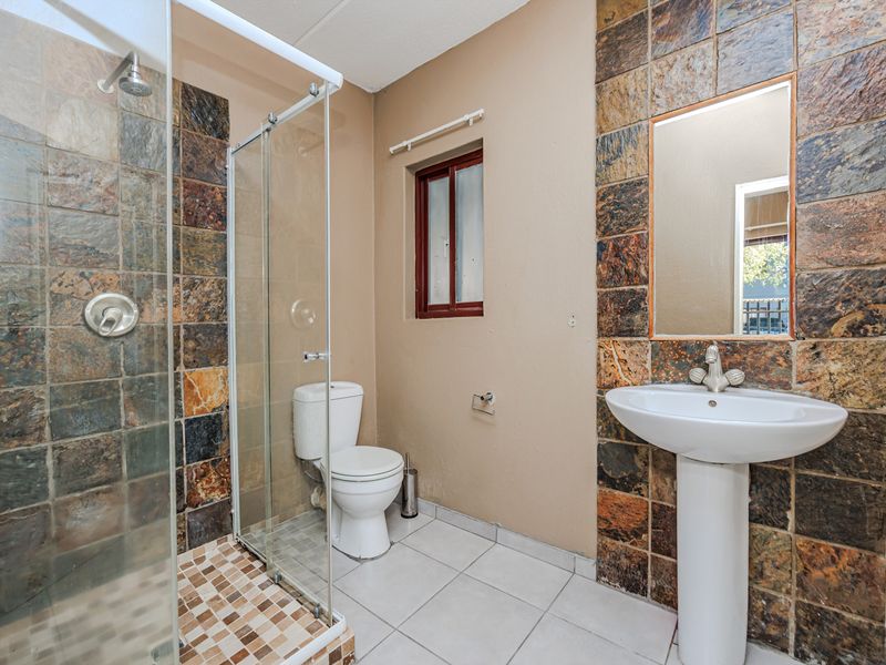 A functional bathroom featuring a glass-enclosed shower, pedestal basin, and distinctive slate wall tiling.
