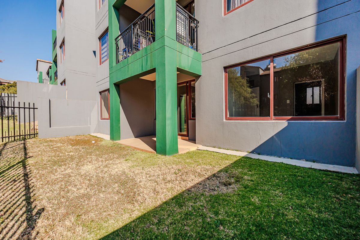 Rear view of the apartment building featuring a ground floor covered patio, sliding glass doors, and a small private garden area with perimeter fencing.