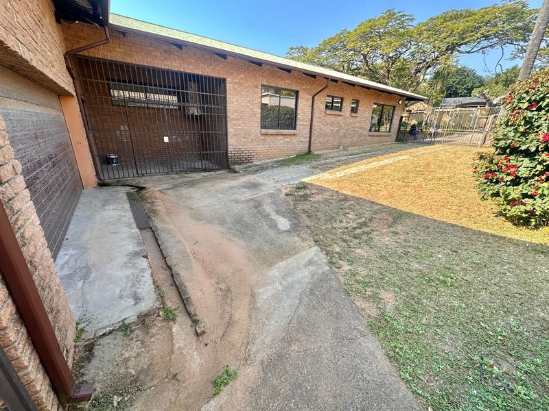 Rear exterior view of a face brick house featuring a concrete driveway, security gate, and a garden area with lawn.