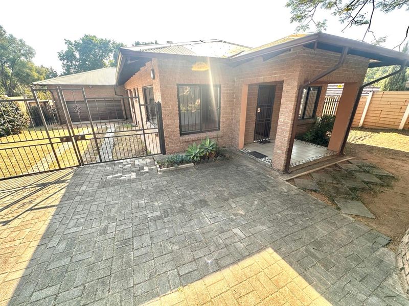 Front view of a face brick house featuring a paved driveway, secure metal gate, and a covered entrance porch with tiled flooring.