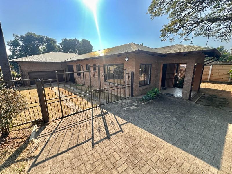 Front exterior view of a single-story brick house featuring a paved driveway, metal security gate, and attached garage.