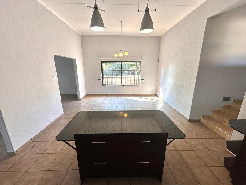 Spacious open-plan living area featuring tiled flooring, a central kitchen island, and natural light through a window with security bars.