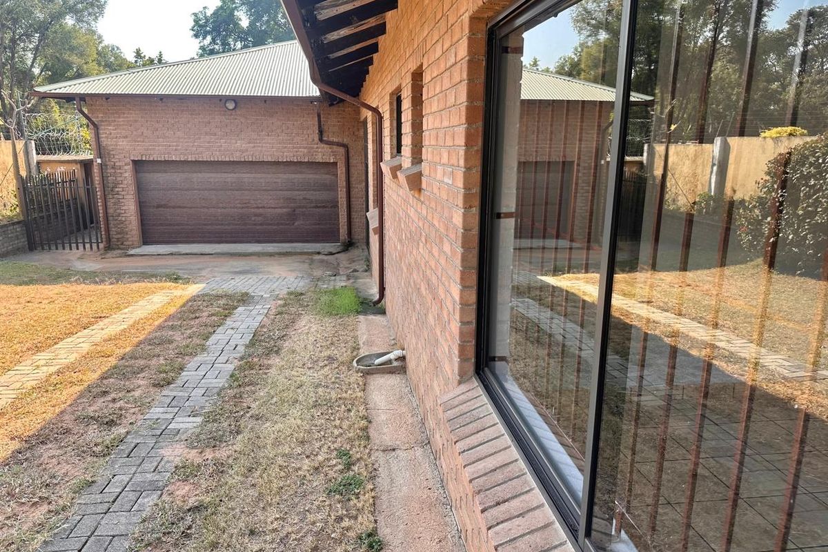 Rear exterior view of the house featuring a brick facade, sliding glass door, paved walkway, and a detached garage.
