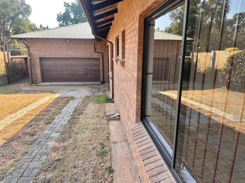 Rear exterior view of the house featuring a brick facade, sliding glass door, paved walkway, and a detached garage.