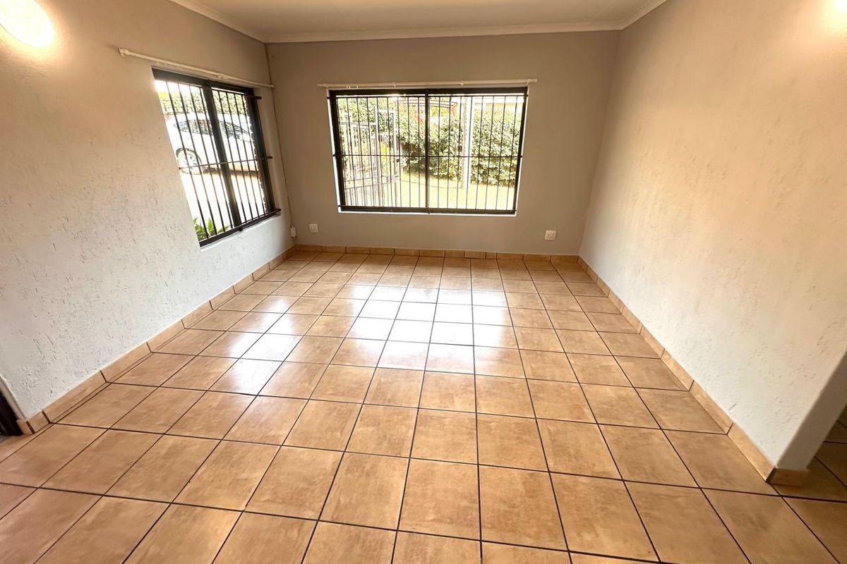 A bright, empty living room featuring neutral walls, ceramic tiled flooring, and windows fitted with security bars.