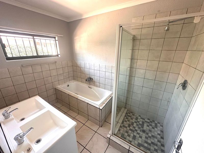 A functional bathroom featuring a built-in bathtub, separate glass-enclosed shower, and a double vanity unit with tiled finishes throughout.