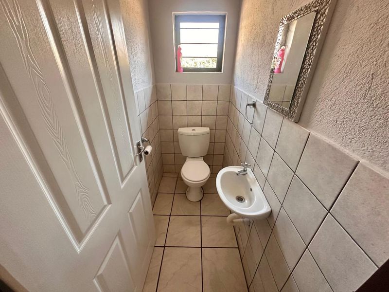 A compact guest bathroom featuring a wall-mounted basin, toilet, and neutral ceramic tiling throughout.