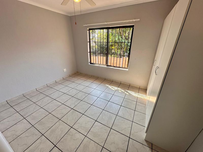 A clean, empty bedroom featuring neutral tiled flooring, a built-in wardrobe, and a ceiling fan, offering a blank canvas for personalization.
