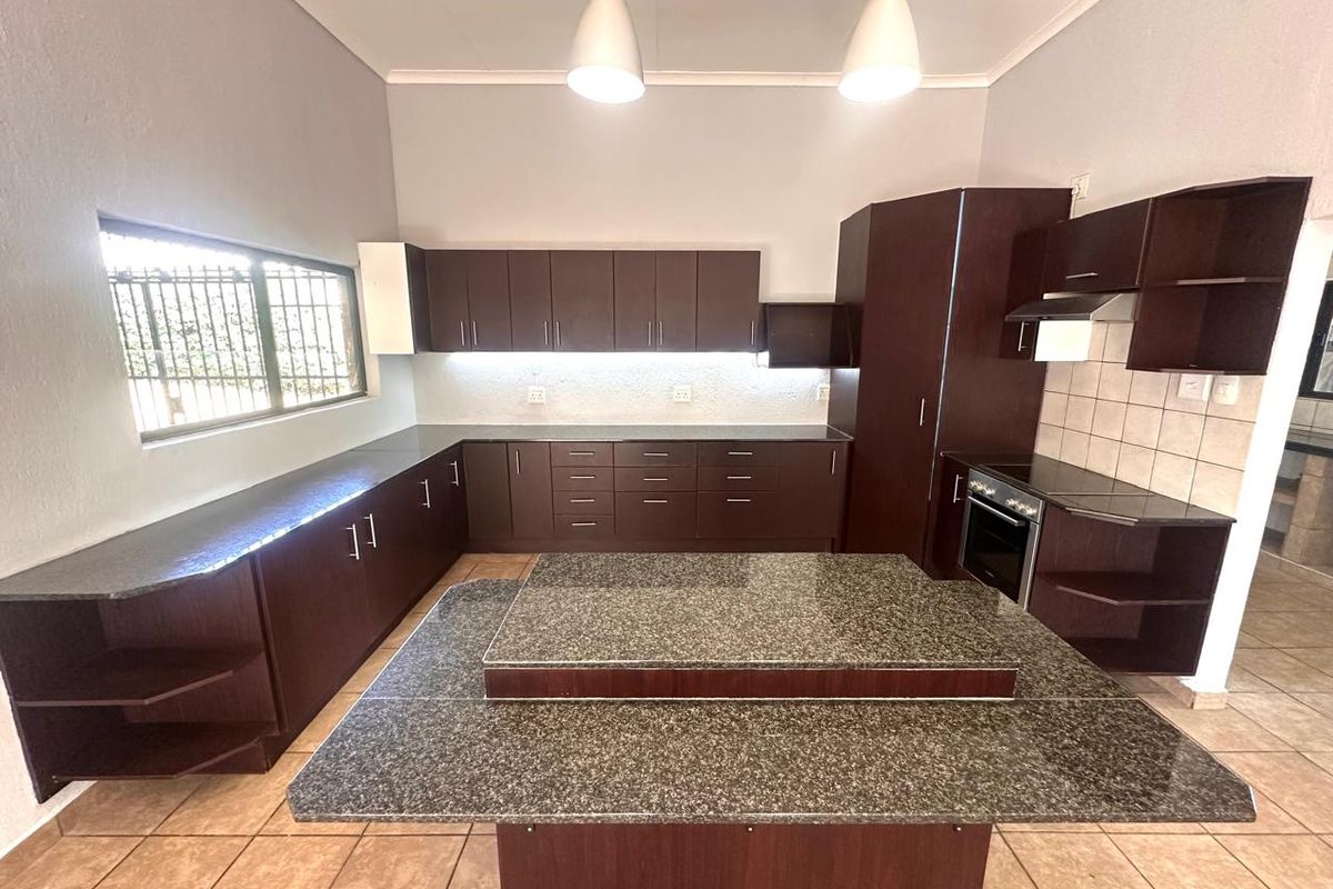 Spacious kitchen featuring dark wood cabinetry, granite countertops, a central island, and built-in oven with extractor fan.