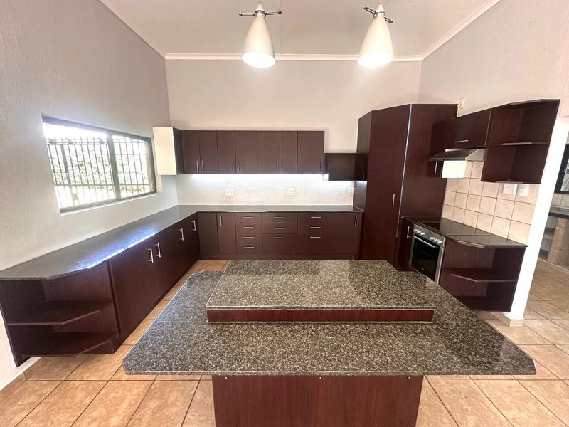 Spacious kitchen featuring dark wood cabinetry, granite countertops, a central island, and built-in oven with extractor fan.