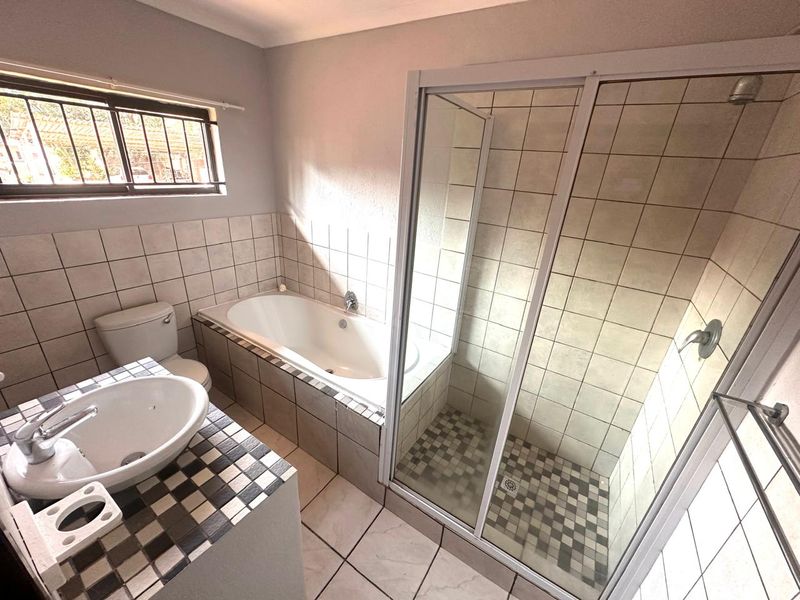A functional bathroom featuring a built-in bathtub, separate shower enclosure, tiled vanity with basin, and neutral wall tiling.