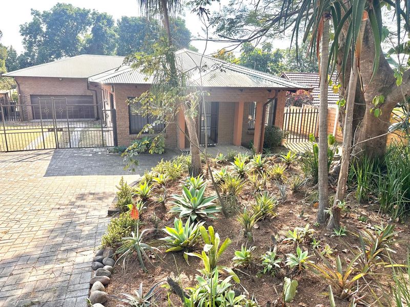 Front view of a brick house featuring a paved driveway, double garage, and a well-maintained landscaped garden with mature trees.