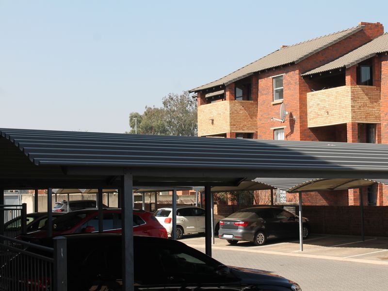 Exterior view of an apartment complex featuring covered parking bays and brick building facades with balconies.