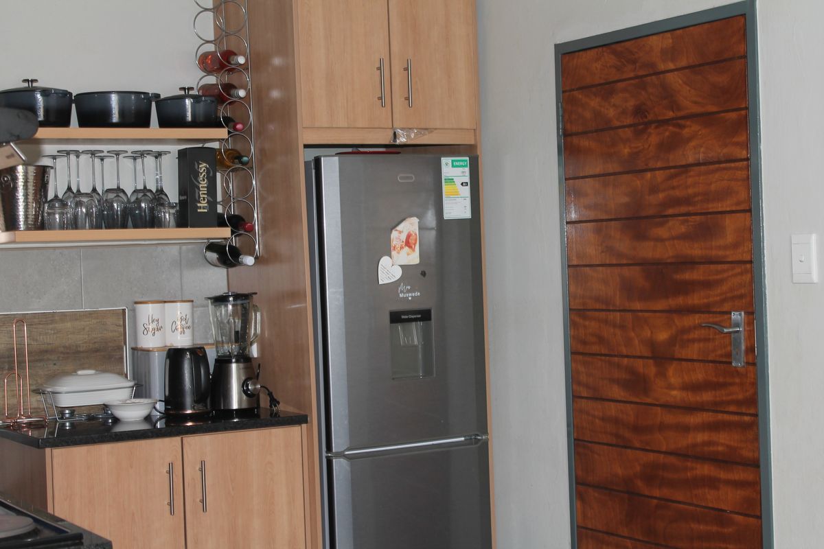 A kitchen area featuring laminate cabinetry, granite countertops, and open shelving, adjacent to a wooden internal door.