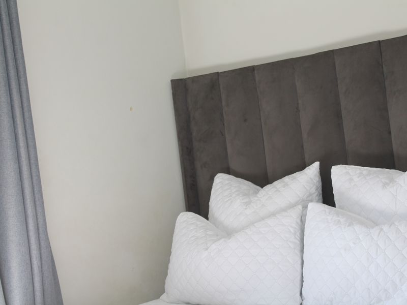 A close-up view of a bedroom corner featuring a dark upholstered headboard and neutral wall finishes.