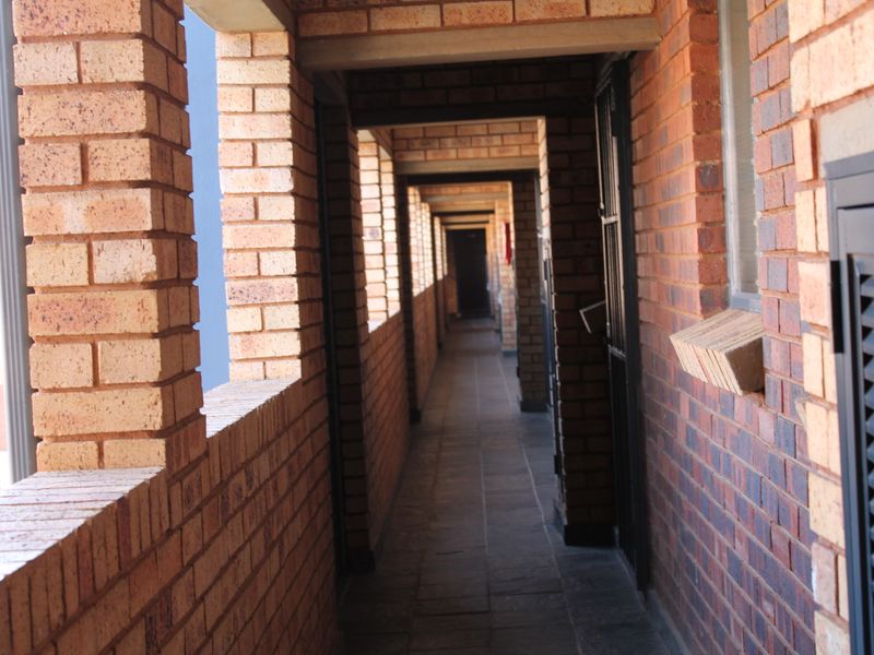 An open-air apartment complex hallway featuring exposed brick walls, tiled flooring, and secure access points.