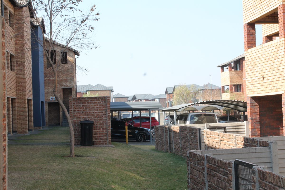 Exterior view of the apartment complex grounds featuring face brick buildings, covered parking bays, and established lawn areas.