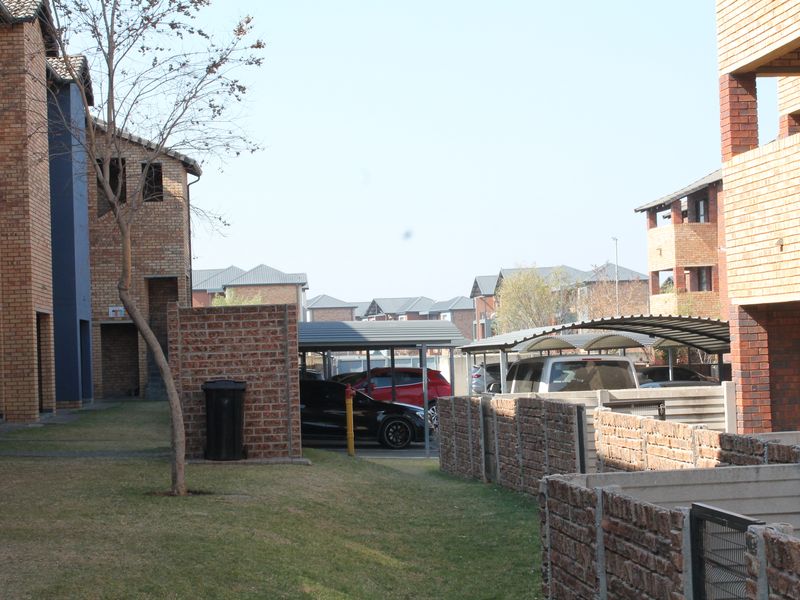 Exterior view of the apartment complex grounds featuring face brick buildings, covered parking bays, and established lawn areas.