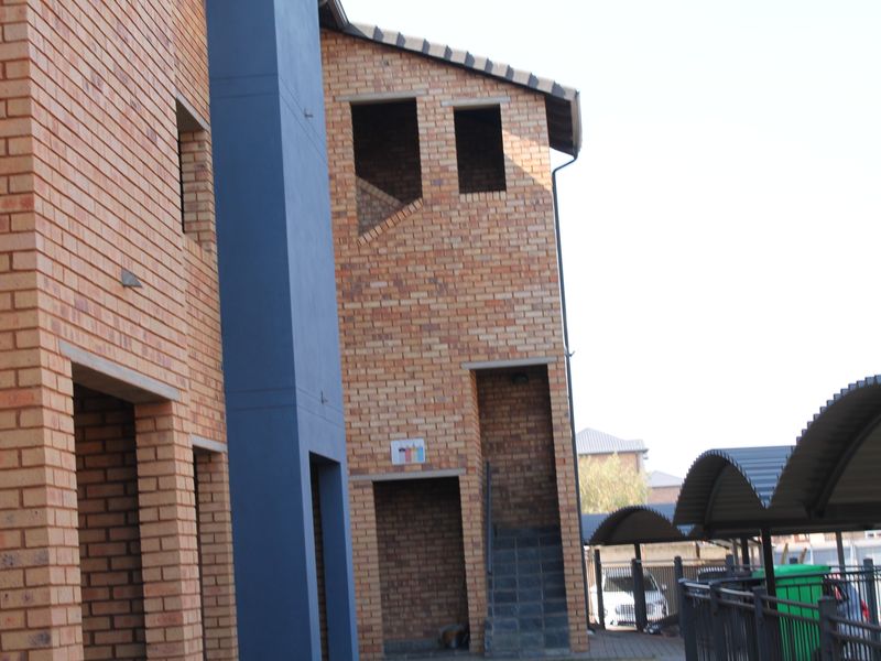 Exterior view of a modern face brick apartment complex featuring covered parking bays and an external staircase.