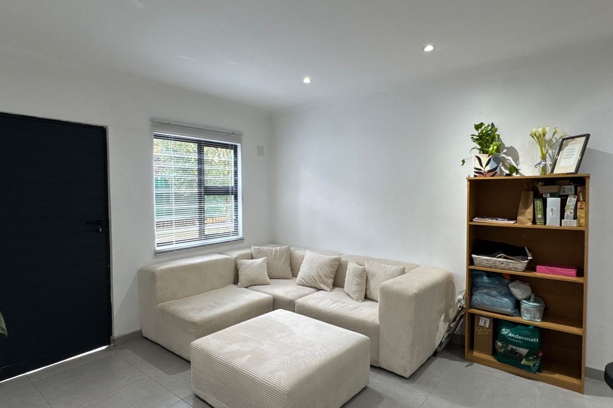 A bright and modern living room featuring neutral tiled flooring, recessed downlighting, and a large window with fitted venetian blinds.