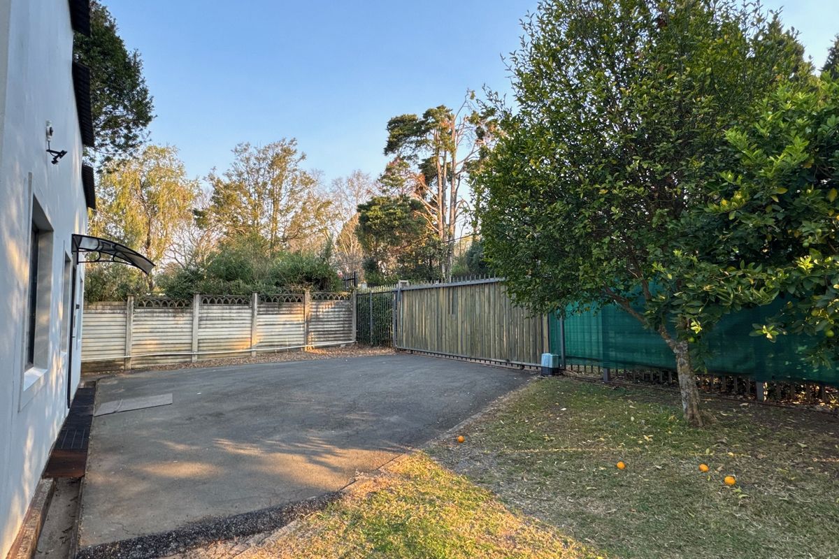 A rear exterior view of the cottage featuring an asphalt driveway, secure perimeter fencing with a timber gate, and a small garden area.