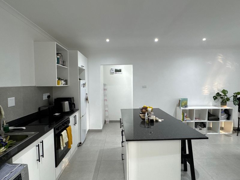 Modern kitchen featuring a central island with granite countertops, white cabinetry, built-in oven, and sleek tiled flooring in an open-plan layout.