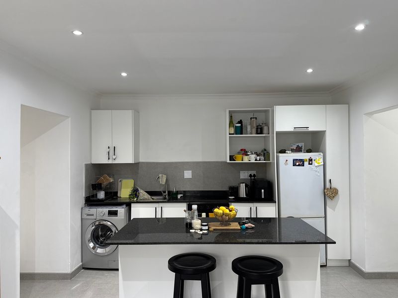 Modern kitchen featuring white cabinetry, dark granite countertops, a central island, and integrated laundry facilities, illuminated by recessed ceiling lighting.