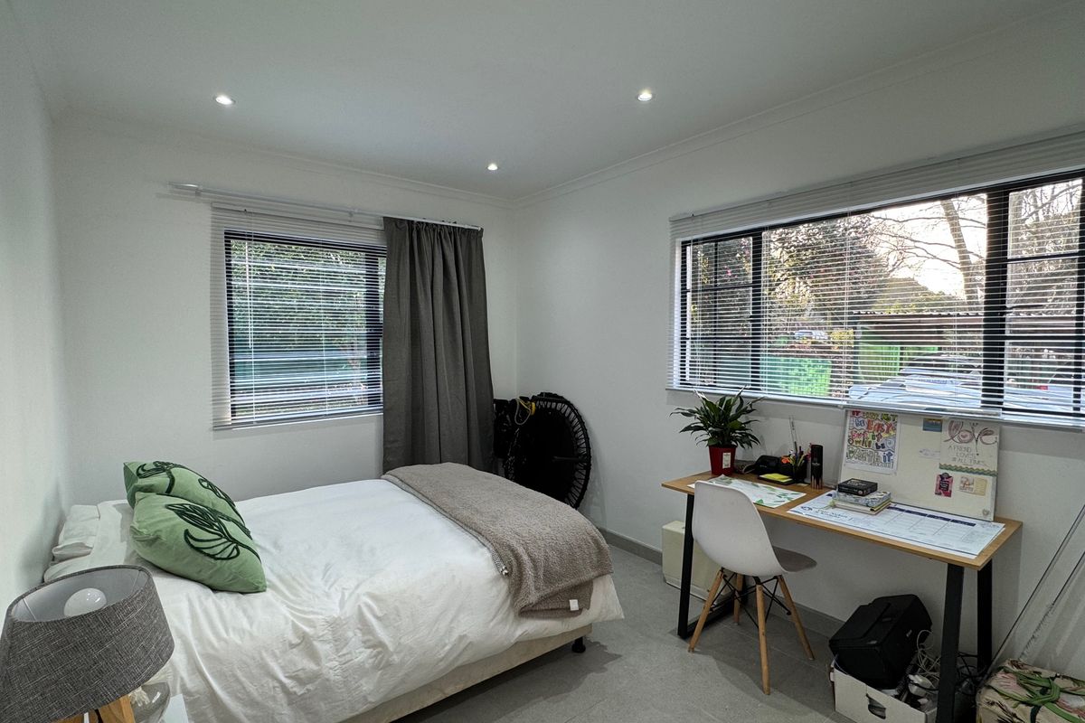 A bright and well-maintained bedroom featuring tiled flooring, recessed downlighting, and dual windows with fitted venetian blinds.