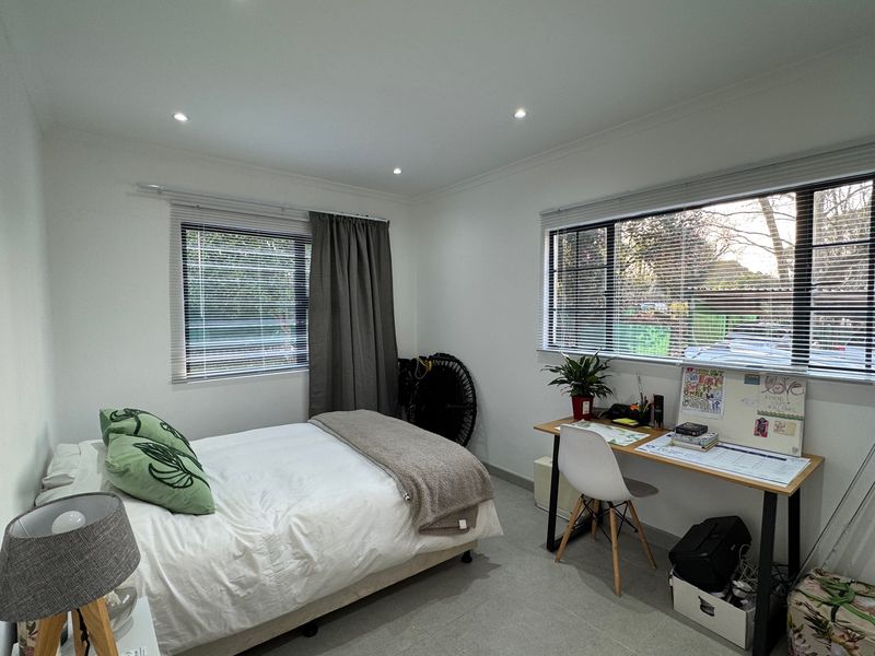 A bright and well-maintained bedroom featuring tiled flooring, recessed downlighting, and dual windows with fitted venetian blinds.