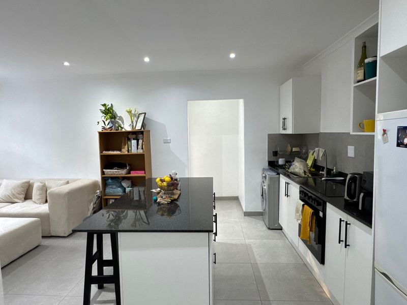 Modern open-plan kitchen featuring a central island with granite countertops, sleek white cabinetry, built-in oven, and tiled flooring, seamlessly integrated with the living area.