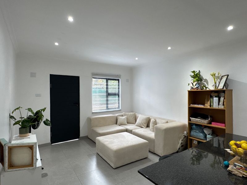 A bright open-plan living area featuring modern tiled flooring, recessed downlighting, and a sleek granite countertop, creating a clean and functional space.