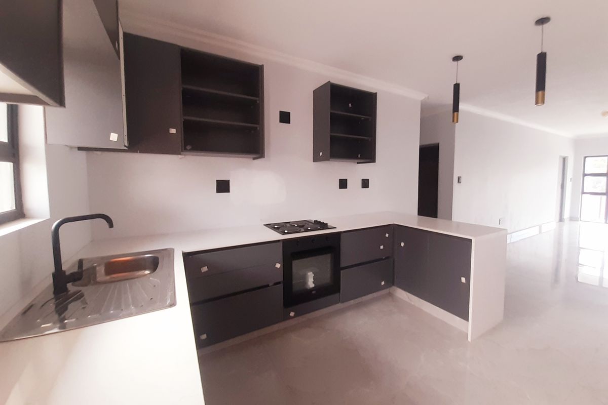 Modern kitchen featuring dark grey cabinetry, white countertops, built-in oven, gas hob, and sleek pendant lighting in an open-plan layout.