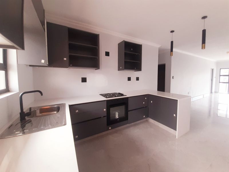 Modern kitchen featuring dark grey cabinetry, white countertops, built-in oven, gas hob, and sleek pendant lighting in an open-plan layout.