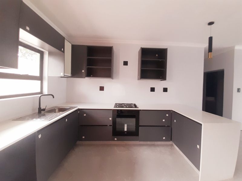 Modern kitchen featuring dark grey cabinetry, white countertops, built-in oven and hob, and a stainless steel sink with a contemporary black faucet.