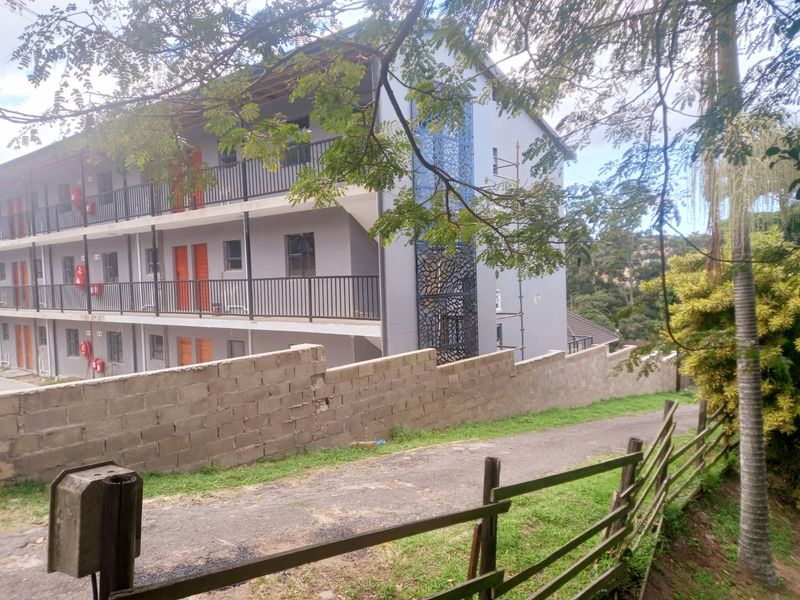 Exterior view of a multi-story apartment building featuring metal balustrades, a decorative screen, and an unfinished concrete block boundary wall.
