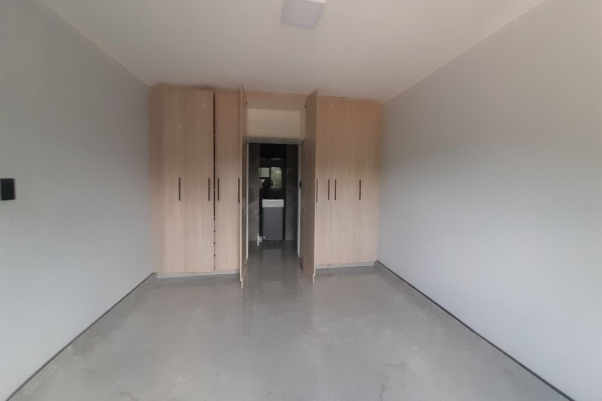An empty bedroom featuring light wood-toned built-in cupboards and neutral tiled flooring, offering a clean and versatile space.