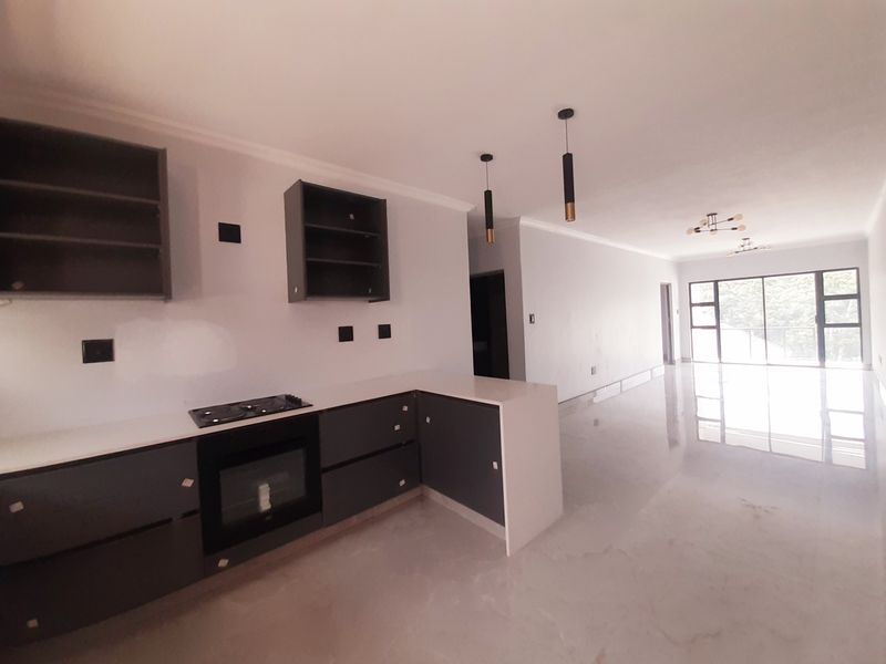Modern open-plan kitchen and living area featuring sleek cabinetry, built-in appliances, stone countertops, and large sliding doors leading to an outdoor space.