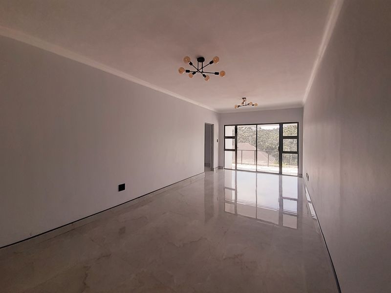 Spacious, empty living area featuring polished porcelain tile flooring, modern light fixtures, and large sliding glass doors leading to an outdoor space.