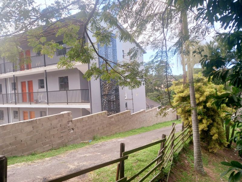 Exterior view of an apartment building featuring metal balcony railings, a decorative screen, and a concrete block boundary wall along the driveway.