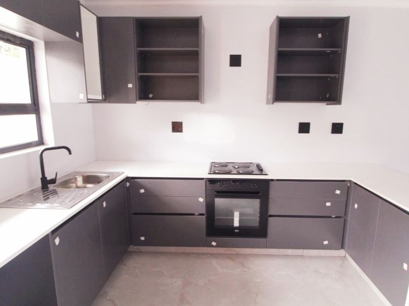 Modern kitchen featuring dark grey cabinetry, white stone countertops, built-in oven, electric hob, and a stainless steel sink with a black mixer tap.
