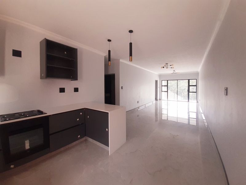 Modern open-plan kitchen and living area featuring sleek cabinetry, built-in appliances, polished tiled floors, and large sliding doors leading to an outdoor space.