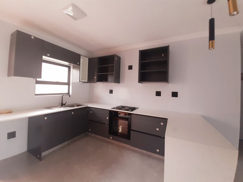 A modern kitchen featuring dark grey cabinetry, stone countertops, built-in oven, and gas hob, currently awaiting final finishing touches on cabinet doors.