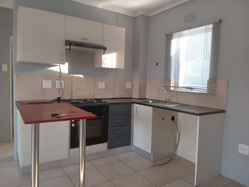 A compact kitchen featuring built-in cabinetry, an electric oven and hob, extractor fan, and tiled splashbacks. The space requires minor repairs and cosmetic updates.