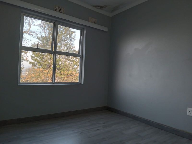 An empty bedroom featuring laminate flooring, grey walls, and an aluminium window, showing visible signs of ceiling water damage.