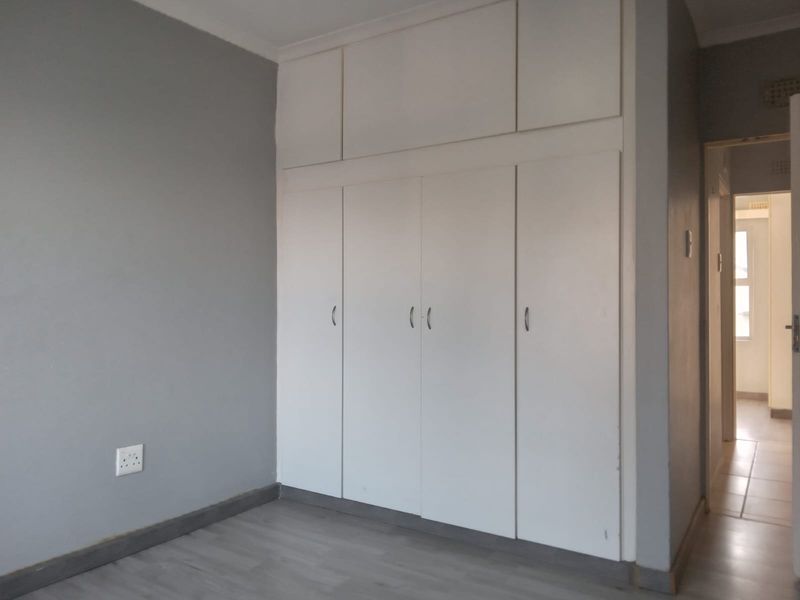 A clean, empty bedroom featuring neutral grey walls, laminate flooring, and floor-to-ceiling built-in cupboards providing ample storage space.